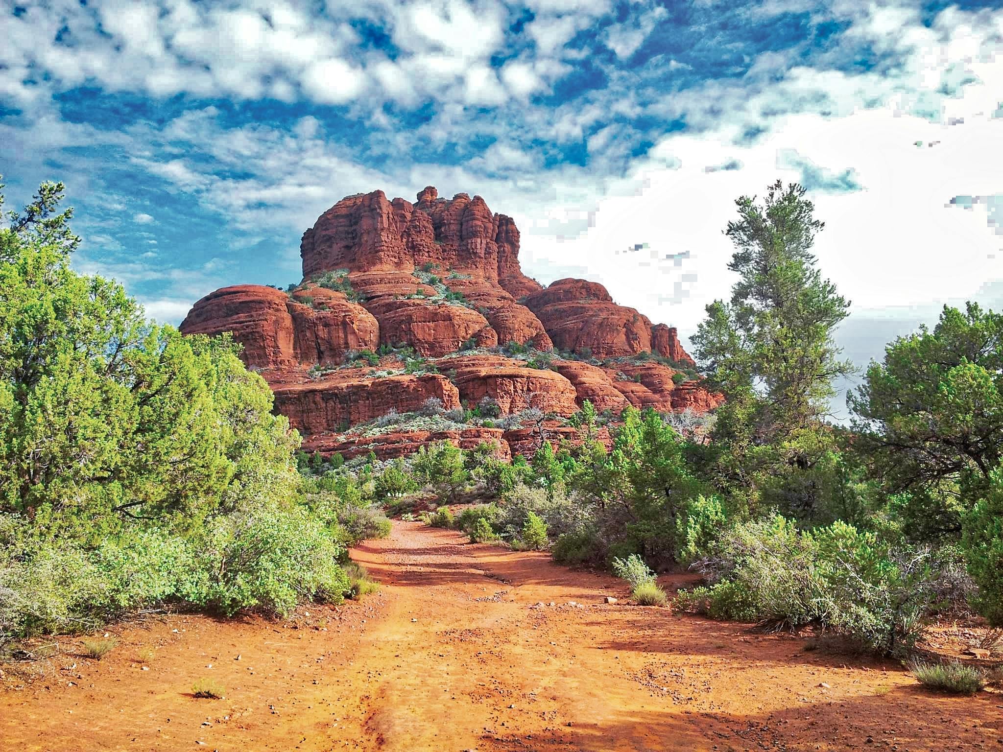 Beautiful red rock formations in Sedona, Arizona, surrounded by lush greenery under a vibrant sky.
